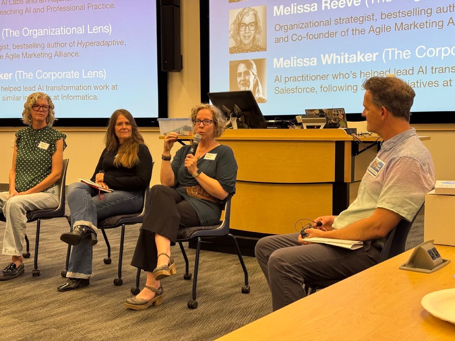Susan Adams speaking into a microphone on a four-person panel at the RMAIIG June meeting in Boulder.